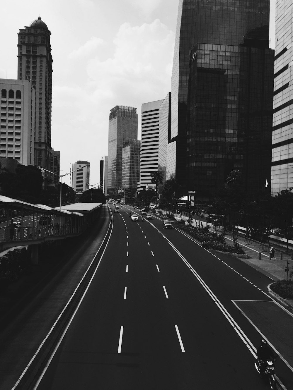 grayscale photo of vehicle running on road under buildings