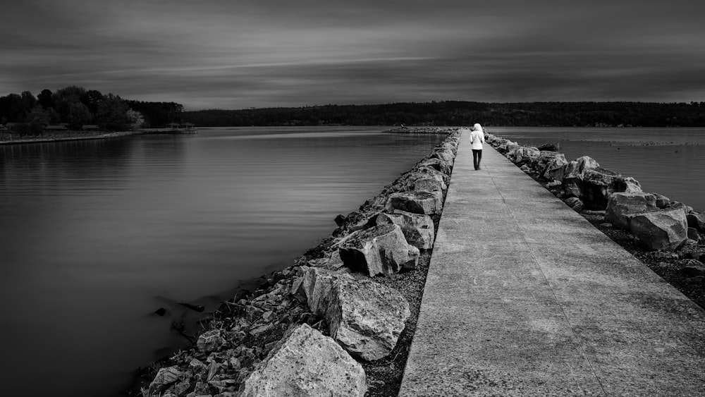 person walking on concrete dock in grayscale photo