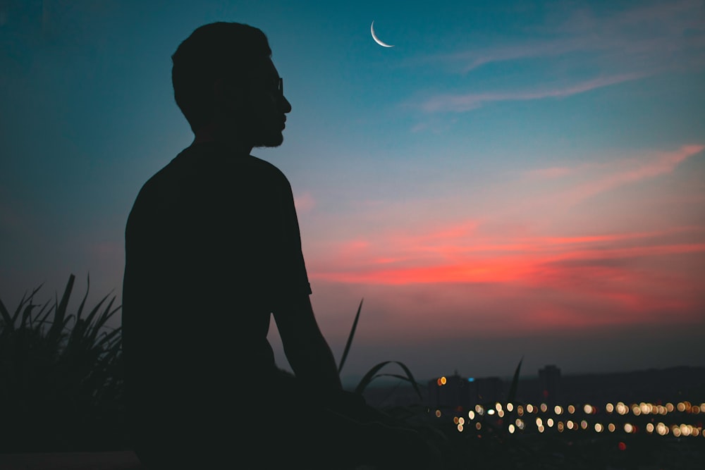 Silhouette eines Mannes auf dem Gipfel eines Hügels mit Blick auf die beleuchtete Stadt in der Morgendämmerung