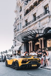 yellow sport car parked on street surrounded group of people