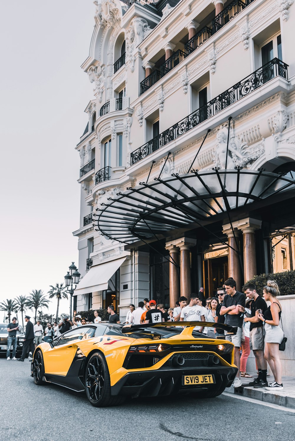 yellow sport car parked on street surrounded group of people