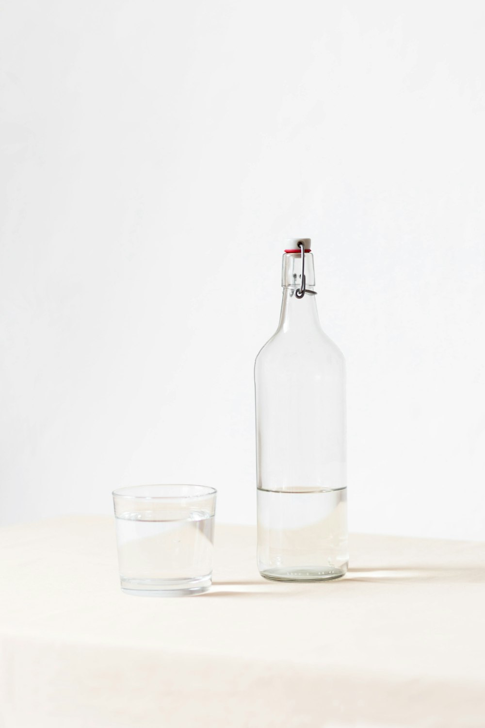 verre de roches à côté d'une bouteille à moitié vide sur une surface blanche