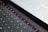 A close-up view of a partially illuminated laptop keyboard. The screen displays lines of code or text in a programming or command-line environment. The keys are dark with bright white lettering, and the text on the screen appears densely packed.