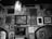Multiple framed pictures and artworks hang on a textured, worn wall in an eclectic arrangement. A prominent light fixture hangs from the ceiling, casting a glow over the artwork, which includes portraits, scene depictions, and abstract pieces.