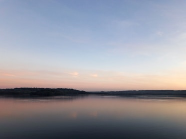 A peaceful scene of a quiet lake at dawn with pastel skies reflecting on the water.