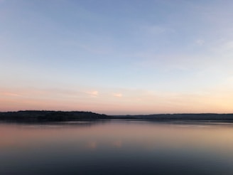 A peaceful scene of a quiet lake at dawn with pastel skies reflecting on the water.