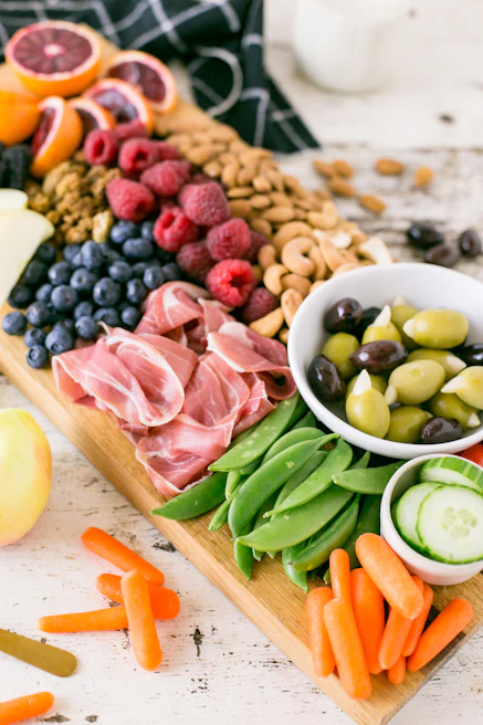 Overhead shot of an elegant grazing board filled with vibrant seasonal fruits, olives, nuts, and artisan crackers set on a white marble surface