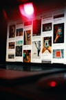 A laptop is displaying a Pinterest-like webpage, showing a grid of various images, including landscapes, close-up shots of hands holding a phone, and artistic photographs. The scene is dimly lit with a prominent red light reflecting off the screen, creating a moody ambiance.
