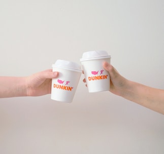 A steaming cup of freshly brewed coffee with a Dunkin' Donuts logo on the cup.