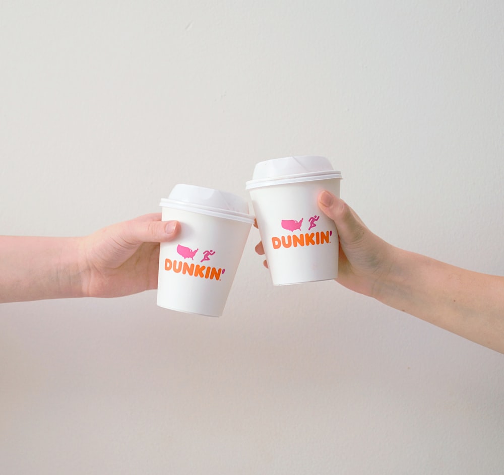 duas pessoas com copos de papel Dunkin' Donuts brancos