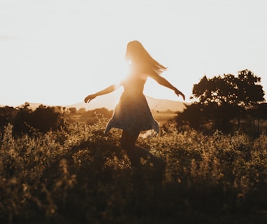 silhouette of woman dancing in the middle of grass field