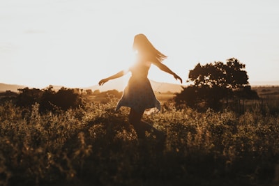 A joyful woman twirling in a colorful maxi dress on a beach at sunset.