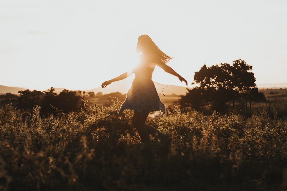 silhouette of woman dancing in the middle of grass field