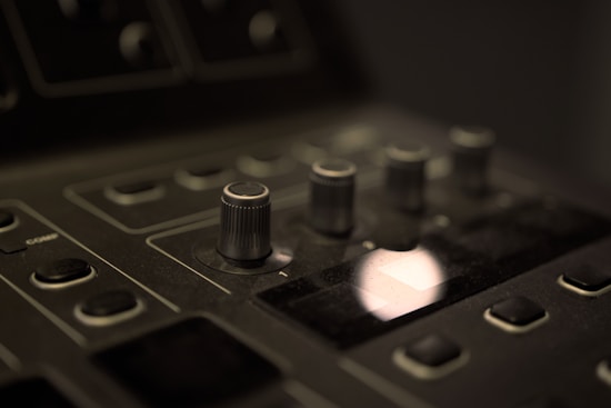A close-up view of a dark-colored electronic control panel featuring several knobs and buttons. The lighting is low and focused, creating a soft glow on the surface.