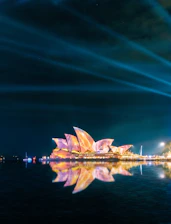 A sleek nighttime cityscape of Sydney with the Opera House illuminated against a deep navy sky.