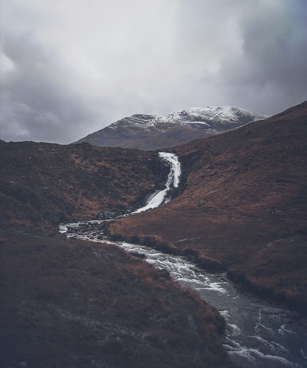 river gushing from mountain under grey cloudy sky