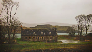brown concrete house in green open field near lake and mountain