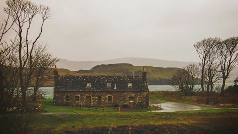 brown concrete house in green open field near lake and mountain