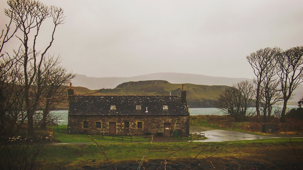 Maison en béton brun dans un champ vert près du lac et de la montagne