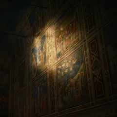 A dimly lit frescoed wall features religious scenes, with figures such as saints and angels depicted in a traditional style. The paintings are illuminated by a focused beam of warm light, highlighting detailed expressions and vivid colors against a darker background.