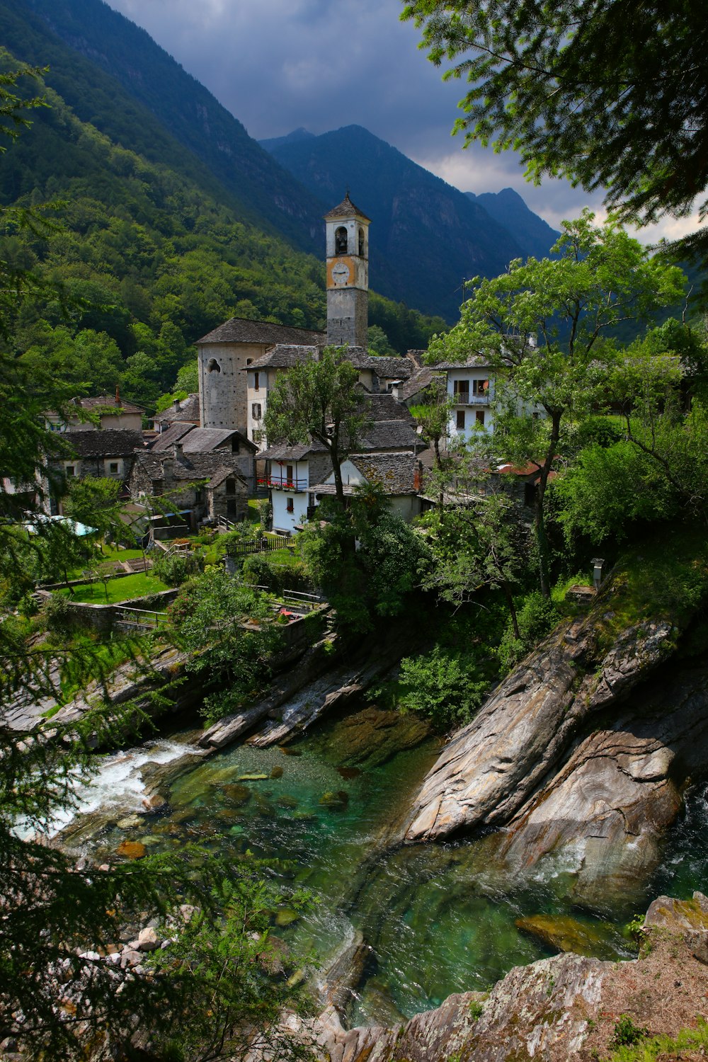 buildings near river, trees, and rocks during day