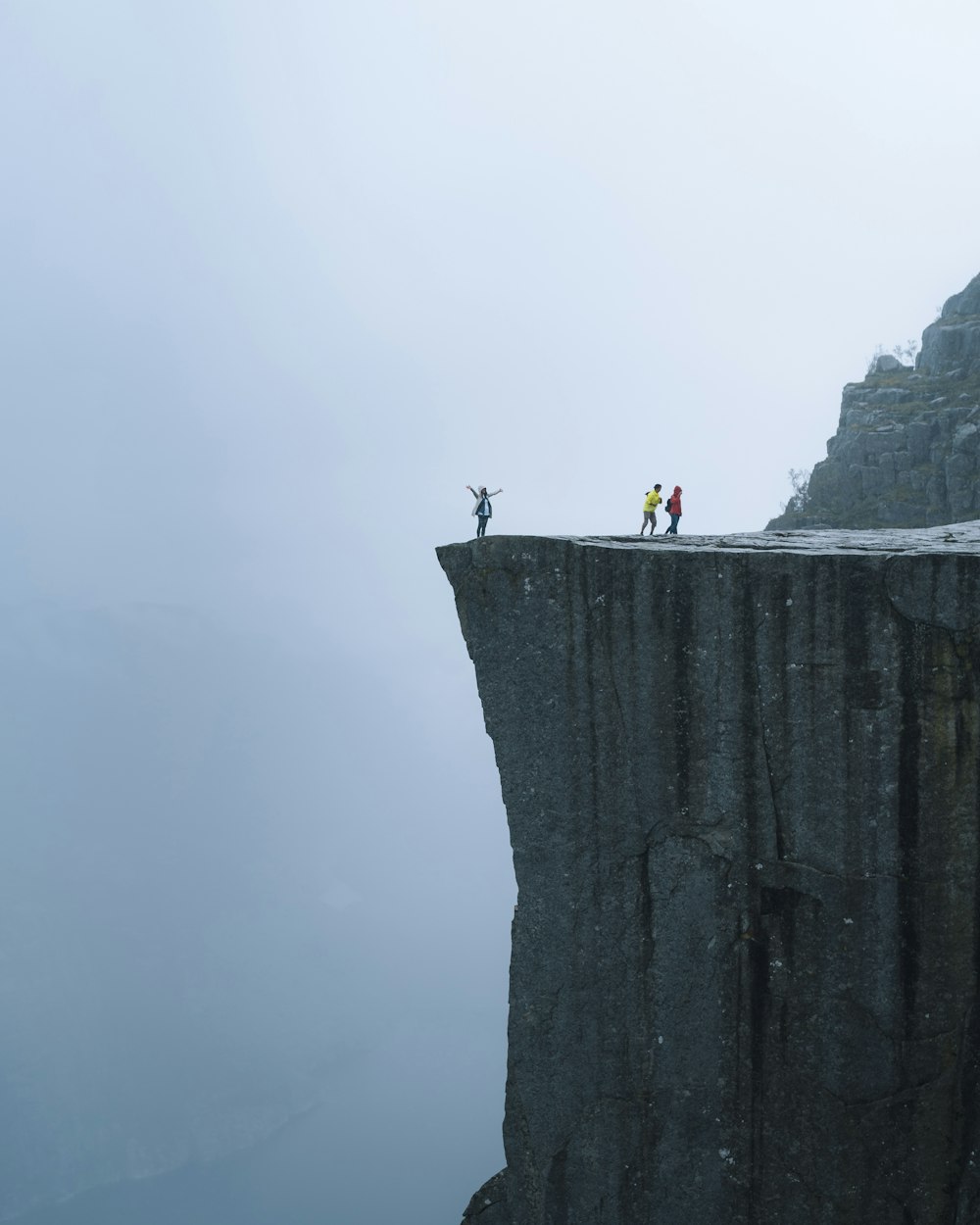 drei Personen, die tagsüber am Rande einer Klippe stehen