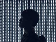 A silhouette of a person is seen against a backdrop of evenly spaced, glowing vertical LED lights that create a dramatic and futuristic effect.