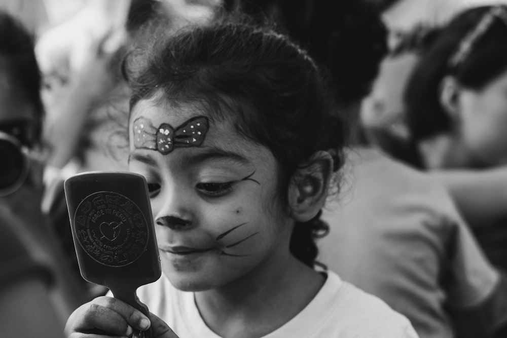 girl with face paint looking at herself on hand mirror
