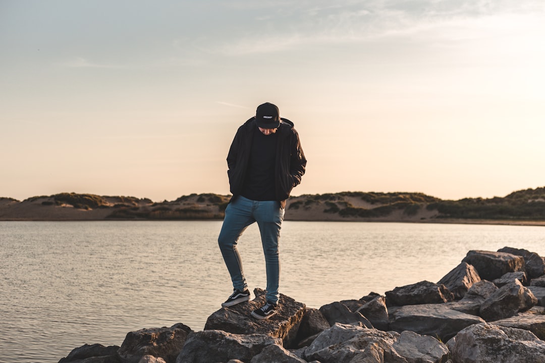 man wearing black zip-up jacket standing on rock