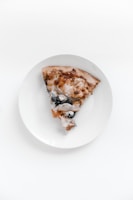 A minimalist plate with a single slice of pizza and a glass of red wine on a dark grey surface.