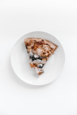 A minimalist plate with a neatly sliced gourmet pizza piece, set against a dark grey background.
