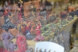A collection of colorful, intricately designed figurines on display in a shop. The figurines include dancers in traditional Spanish attire, such as flamenco dresses with polka dots. There are also other animal figurines like frogs displayed alongside them. The scene is vibrant with a variety of poses indicating movement and celebration.