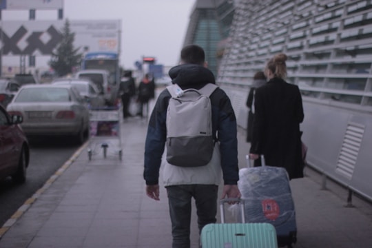 A smiling traveler carrying a suitcase with a package attached, walking through a busy city street.