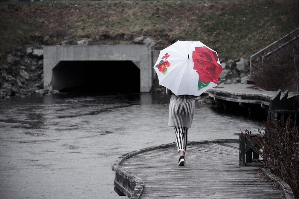 Frau, die neben Wasser geht, während sie einen Regenschirm hält