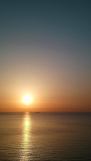 A serene sunrise over a calm ocean with a cruise ship sailing gently in the distance.