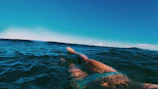 A triathlete swimming in open water with a sunrise backdrop.