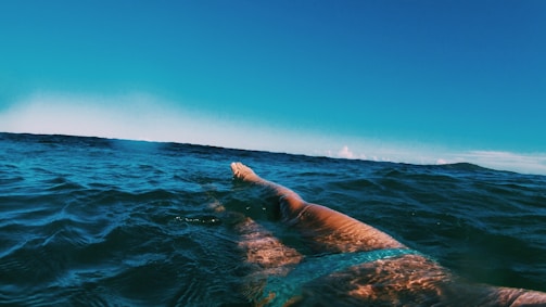 Athletes swimming powerfully in deep open water under a bright sky.
