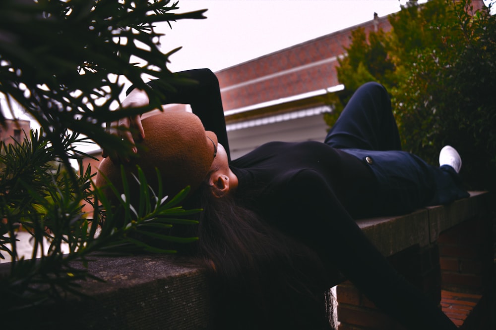 woman wearing black long-sleeved shirt lying on concrete bench