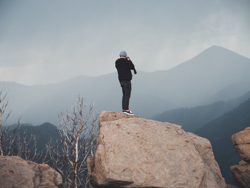 person in black jacket standing on large boulder