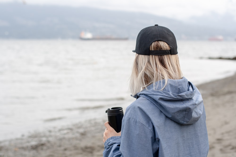 woman standing beside beach while holding black tumbler
