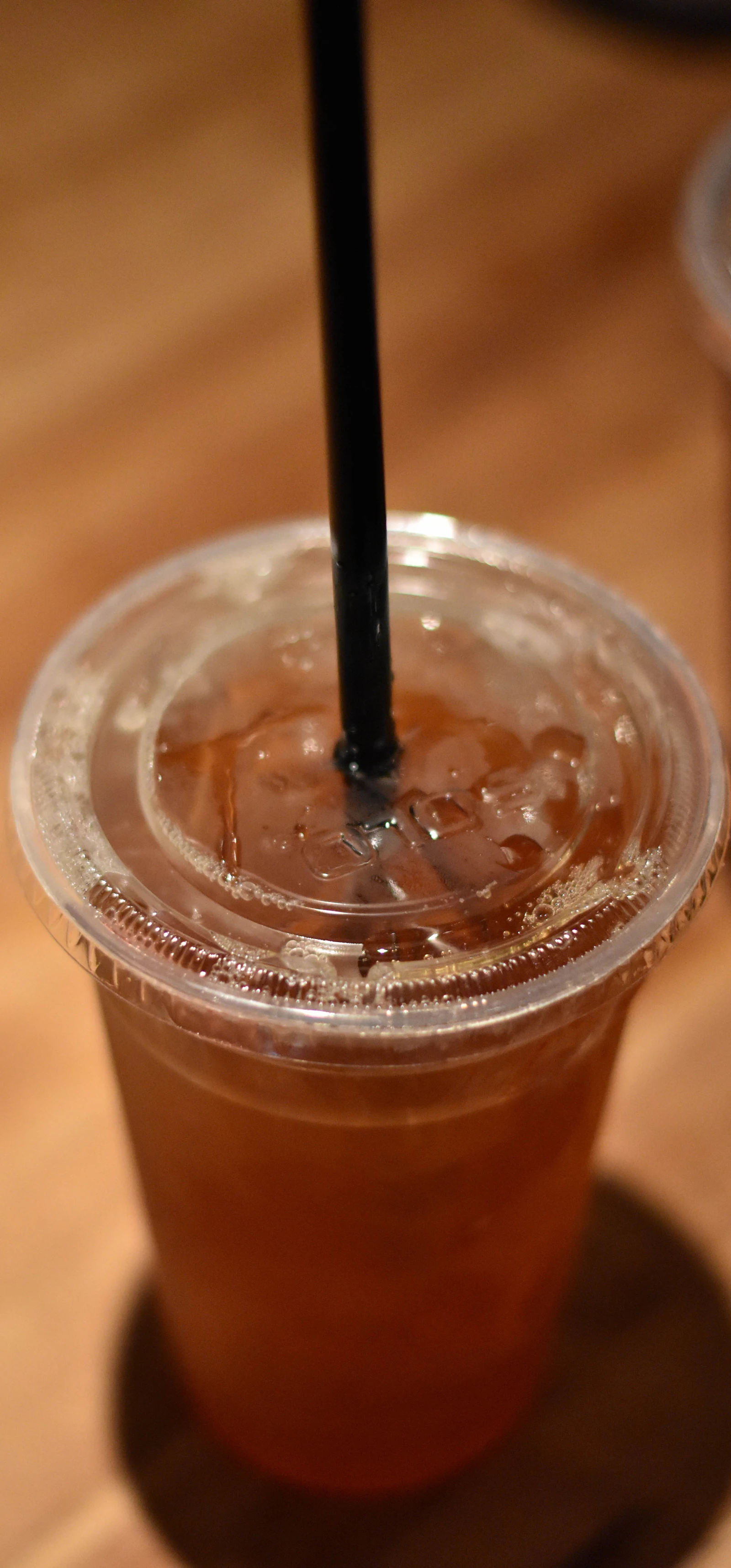 A clear takeaway cup of iced tea with a dome lid and a wide straw