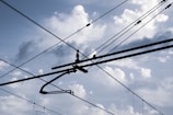 Overhead electrical wires crisscross against a backdrop of a cloudy sky, with various cables and connectors visible.