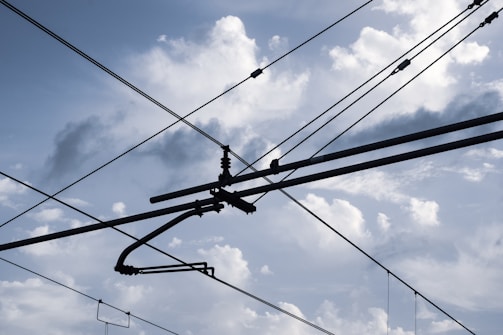 Overhead electrical wires crisscross against a backdrop of a cloudy sky, with various cables and connectors visible.