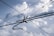 Overhead electrical wires crisscross against a backdrop of a cloudy sky, with various cables and connectors visible.