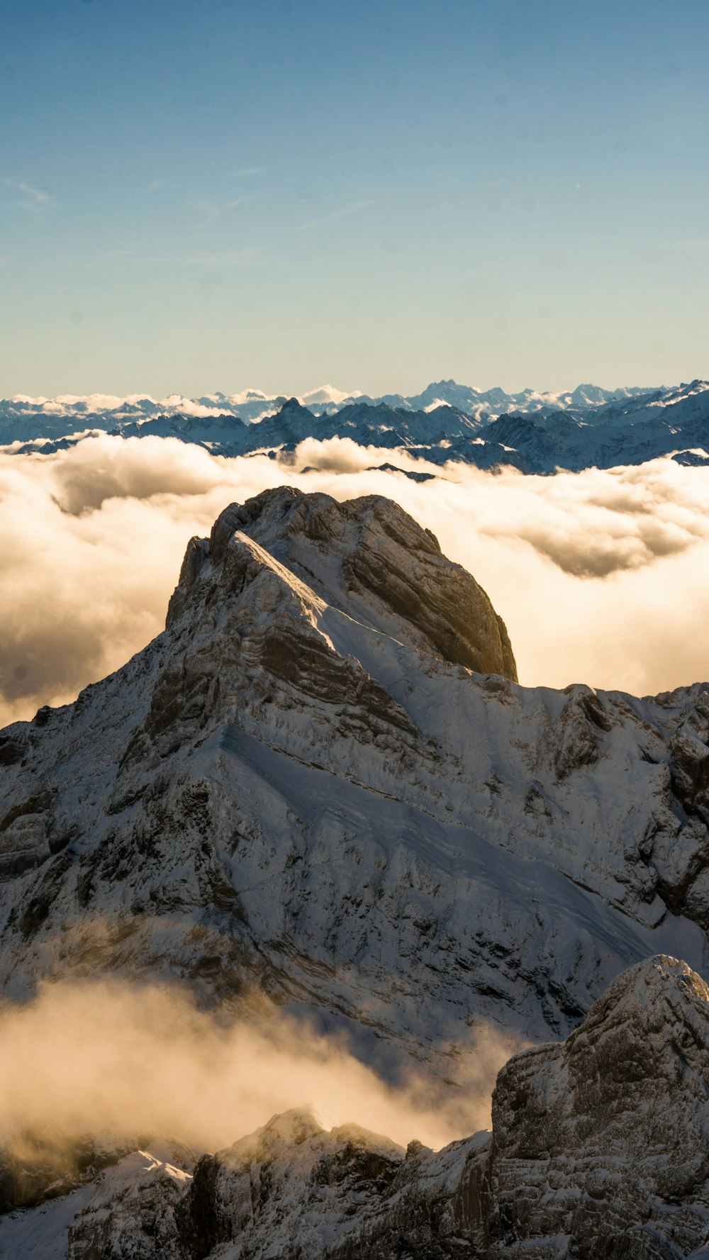 a mountain covered in snow and clouds under a blue sky