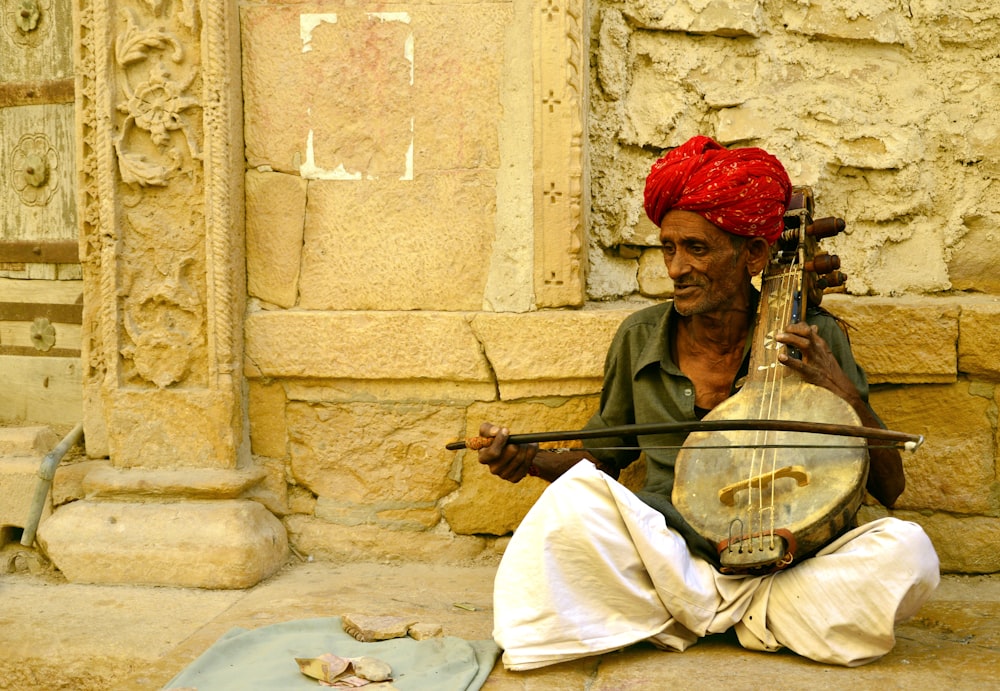 homme portant une coiffe de hijab rouge jouant d’un instrument de musique