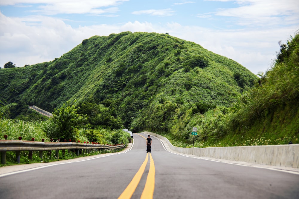 person standing in the middle of road viewing trees