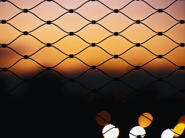A secure perimeter fence with metal mesh surrounding a government building at sunset.