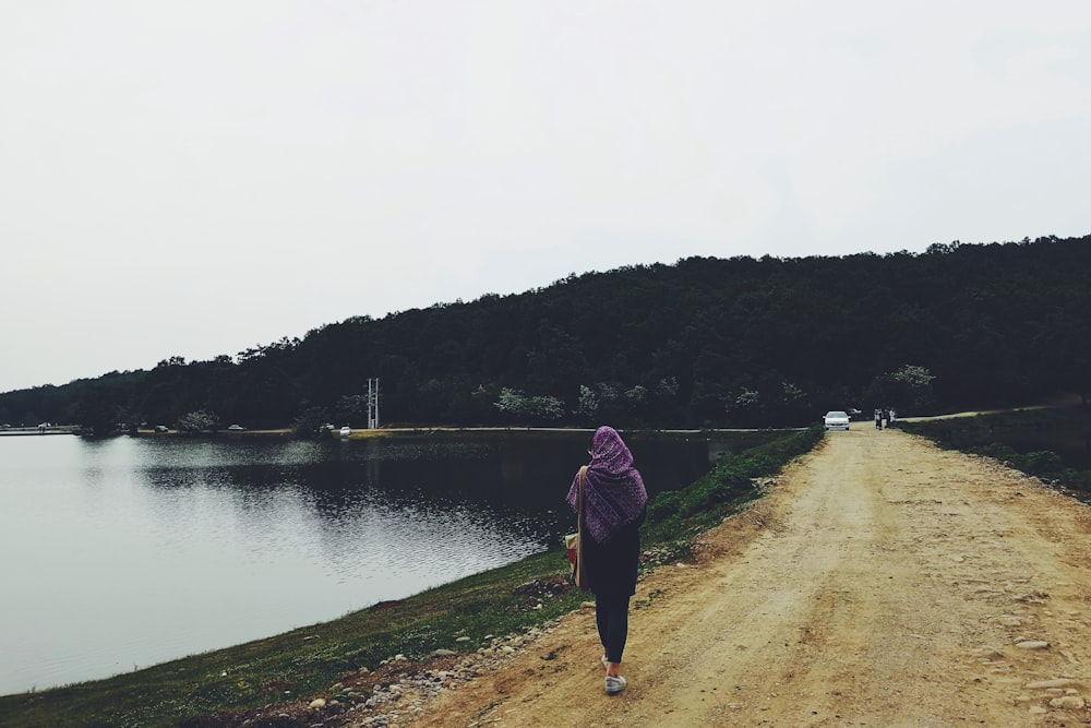 woman walking while overlooking body of water during daytime