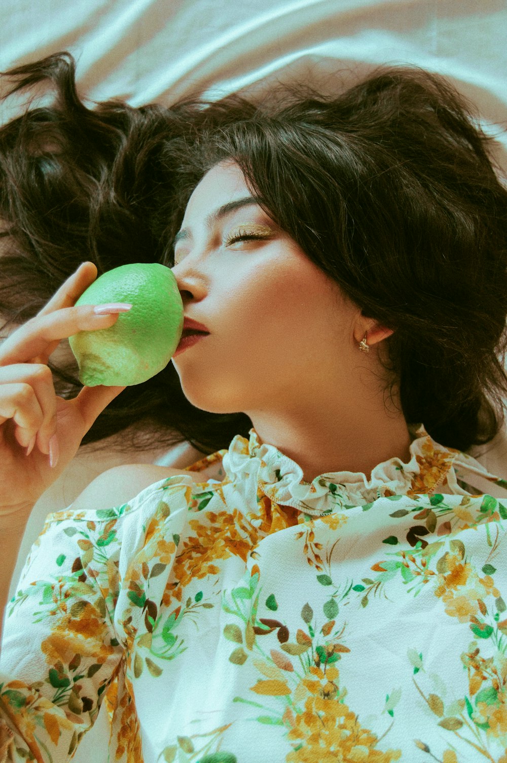 woman smelling on fruit while lying on white surface